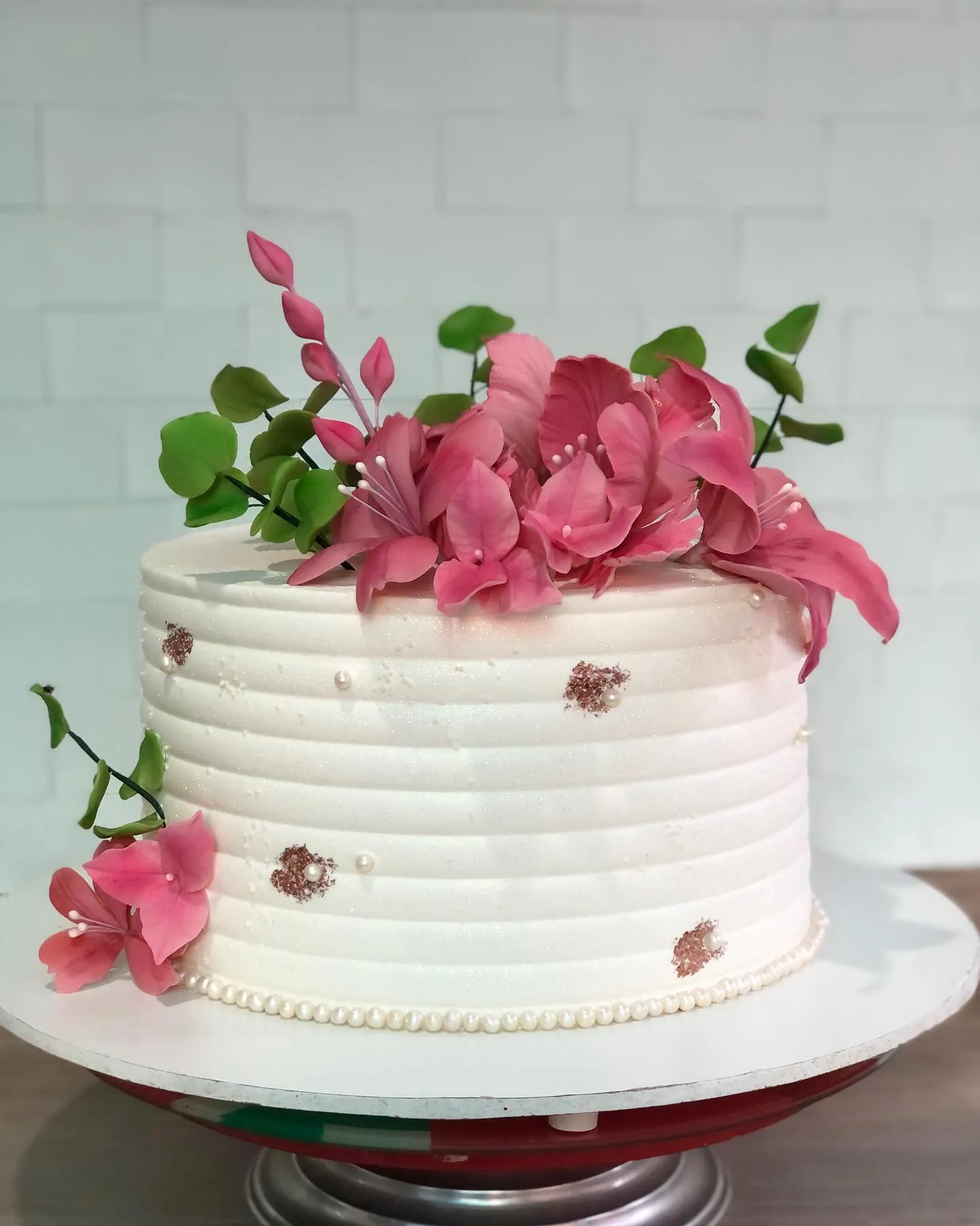Bolo branco redondo de um andar em um suporte, decorado com flores de açúcar rosa vibrante, pérolas e toques de ouro rosé.