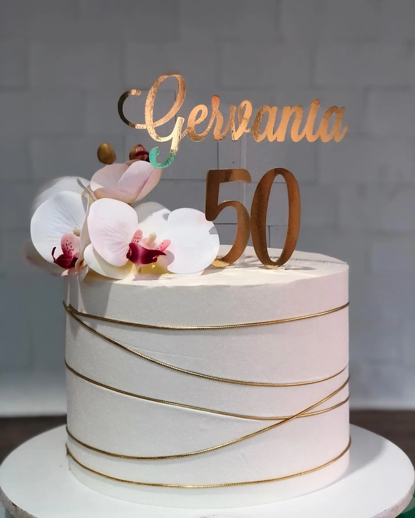 Bolo de aniversário branco de um andar com fios dourados, topper espelhado e um arranjo de orquídeas brancas e rosas.