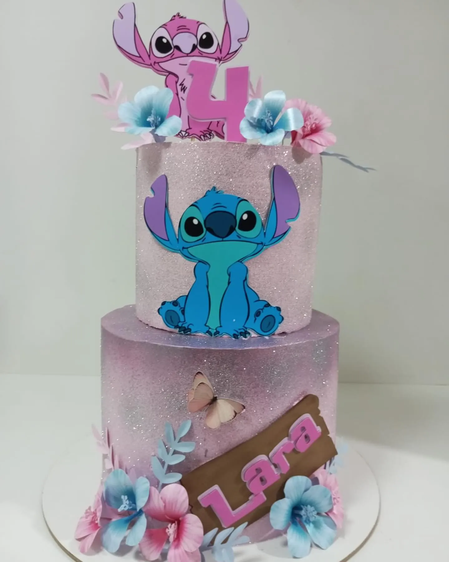 Bolo de festa de dois andares com cobertura rosa e lilás. No topo, as figuras do Stitch e da Angel ao lado do número quatro.