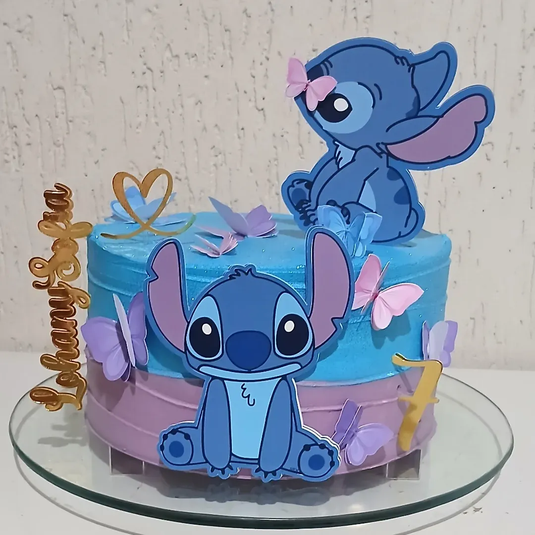 Bolo de festa do Stitch com cobertura em azul e lilás, decorado com apliques do boneco, borboletas e detalhes dourados.